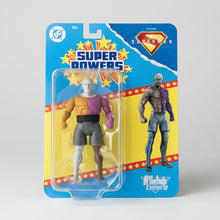 A DC Comics Superman action figure in its original blister card packaging, featuring the character with a white head, purple and orange body, and gray shorts, alongside a larger printed figure on the card.